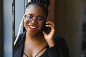 Smiling dark skinned woman in trendy wear laving cafe talking on mobile phone via roaming tariffs,african american millennial female walking and making smartphone call satisfied with connection photo