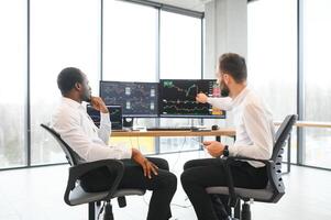 Two successful trader sitting in office, checking cryptocurrency information data on finance market graph, pointing on monitor photo