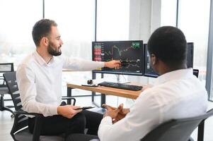 Two successful trader sitting in office, checking cryptocurrency information data on finance market graph, pointing on monitor photo
