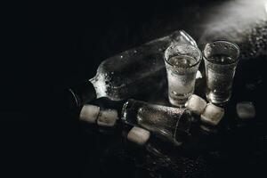Close-up view of bottle of vodka with glasses standing on ice on black. photo
