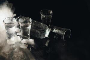 Close-up view of bottle and glasses of vodka standing isolated on black. photo