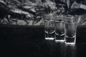 Vodka shots with ice on black table, copy space. photo