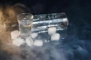 Close-up view of bottle of vodka with glasses standing on ice on black. photo