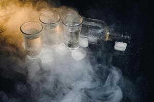 Close-up view of bottle and glasses of vodka standing isolated on black. photo
