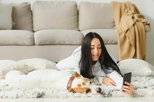Portrait of beautiful young woman with her dog using mobile phone at home photo