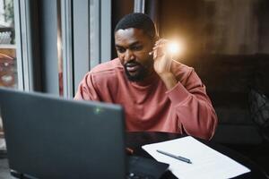 Afro american talks chat on computer sits in cafe with cup of coffee. Black man calls on laptop on link and speaks. He wears in shirt and suit jacket. link online connection photo