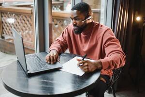 Afro american talks chat on computer sits in cafe with cup of coffee. Black man calls on laptop on link and speaks. He wears in shirt and suit jacket. link online connection photo
