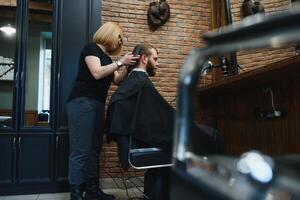 Professional hairdresser woman doing styling of handsome guy with electric hair clipper at barber shop photo