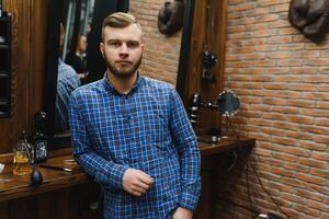 Perfection. Handsome bearded man at barbershop. Portrait of stylish young guy in jacket touching his hair while visiting barbershop or salon. Mens haircut. Barbershop concept photo