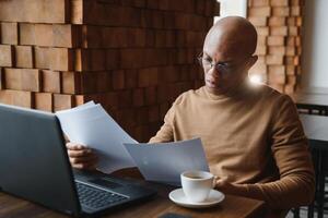 Portrait of smiling African American man in glasses sit at desk in office working on laptop, happy biracial male worker look at camera posing, busy using modern computer gadget at workplace. photo