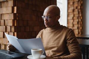 Portrait of smiling African American man in glasses sit at desk in office working on laptop, happy biracial male worker look at camera posing, busy using modern computer gadget at workplace. photo