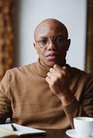 African-Ameican entrepreneur wearing shirt with rolled up sleeves looking through window with thoughtful and serious face expression, feeling nervous before meeting with business partners at cafe. photo