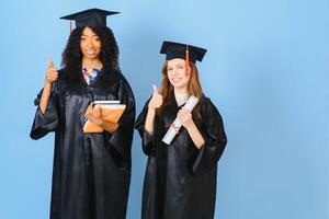 Two girls are posing for take photo in black gowns and hold diploma certificate. They are graduates and hold diploma certificate. They are happy and in good mood.