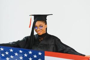 Charming female student smiling in eyeglasses wearing black mantle and standing with American flag photo