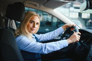 Portrait of a beautiful mature business woman driving a car, sitting behind steering wheel, looking at camera and smiling photo