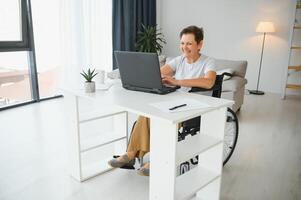 Freelancer in wheelchair using laptop near notebook and papers on table photo