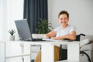 Freelancer in wheelchair using laptop near notebook and papers on table photo