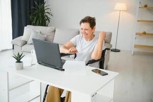 Freelancer in wheelchair using laptop near notebook and papers on table photo