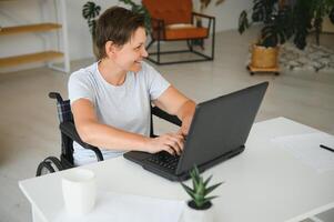 Freelancer in wheelchair using laptop near notebook and papers on table photo