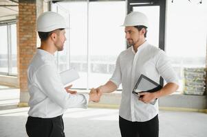 A front view of two smart architects with white helmets reviewing blueprints at a construction site on a bright sunny day photo