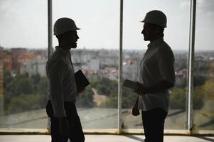 A front view of two smart architects with white helmets reviewing blueprints at a construction site on a bright sunny day photo