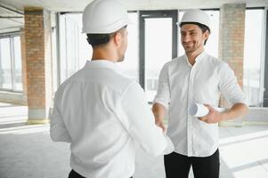 A front view of two smart architects with white helmets reviewing blueprints at a construction site on a bright sunny day photo