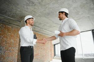 A front view of two smart architects with white helmets reviewing blueprints at a construction site on a bright sunny day photo