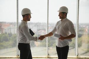 A front view of two smart architects with white helmets reviewing blueprints at a construction site on a bright sunny day photo