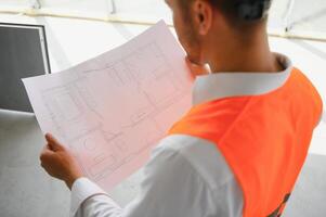 Portrait of an architect builder studying layout plan of the rooms, serious civil engineer working with documents on construction site, building and home renovation, professional foreman at work. photo