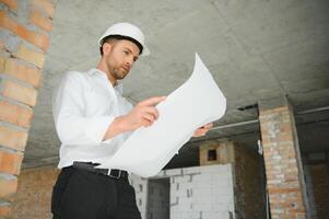 Portrait of an architect builder studying layout plan of the rooms, serious civil engineer working with documents on construction site, building and home renovation, professional foreman at work. photo