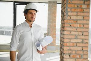 Portrait of an architect builder studying layout plan of the rooms, serious civil engineer working with documents on construction site, building and home renovation, professional foreman at work. photo