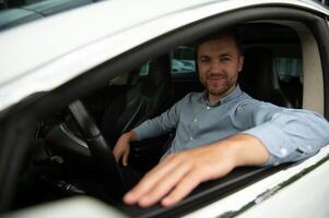 Man of style and status. Handsome young man in full suit smiling while driving a car. photo