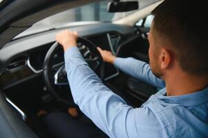 Man of style and status. Handsome young man in full suit smiling while driving a car. photo
