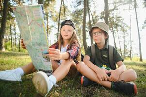 Two happy children having fun during forest hike on beautiful day in pine forest. Cute boy scout with binoculars during hiking in summer forest. Concepts of adventure, scouting and hiking tourism photo
