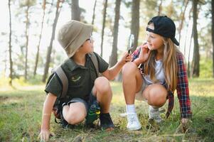 Two happy children having fun during forest hike on beautiful day in pine forest. Cute boy scout with binoculars during hiking in summer forest. Concepts of adventure, scouting and hiking tourism photo