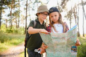 Happy excited school children with backpacks in casual clothes enjoying walk in forest on sunny autumn day, two active kids boy and girl running and playing together during camping trip in nature. photo