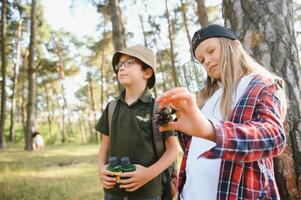 Two happy children having fun during forest hike on beautiful day in pine forest. Cute boy scout with binoculars during hiking in summer forest. Concepts of adventure, scouting and hiking tourism photo