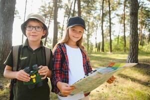 Two happy children having fun during forest hike on beautiful day in pine forest. Cute boy scout with binoculars during hiking in summer forest. Concepts of adventure, scouting and hiking tourism photo