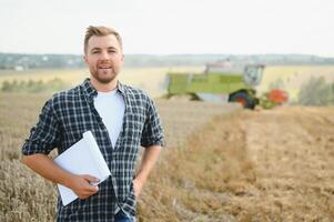 Handsome farmer with tablet standing in front of combine harvester during harvest in field. photo
