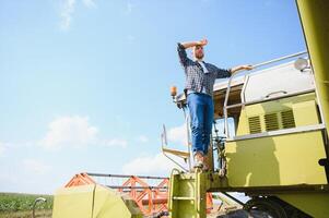 Harvester machine driver climbing into a cab to harvest his wheat field. Farmer getting in combine on ladder holding railing. Agronomist. Rancher after harvesting work photo
