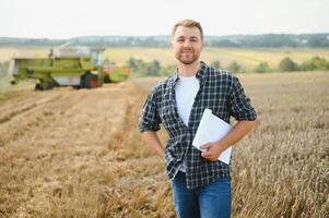 Handsome farmer with tablet standing in front of combine harvester during harvest in field. photo