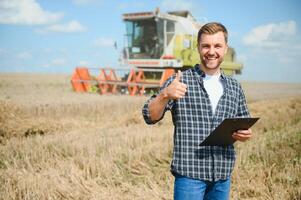 Handsome farmer with tablet standing in front of combine harvester during harvest in field. photo