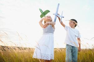 Running boy and girl holding two green and blue airplanes toy in the field during summer sunny day photo