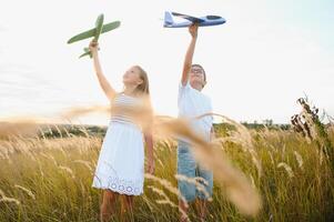 Running boy and girl holding two green and blue airplanes toy in the field during summer sunny day photo