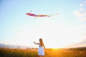 Little cute 7 years old girl running in the field with kite on summer day photo