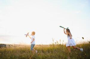 Running boy and girl holding two green and blue airplanes toy in the field during summer sunny day photo