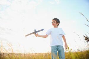 The kid runs with a toy plane. Son dreams of flying. Happy child, boy, runs on the sun playing with a toy airplane on the summer field photo