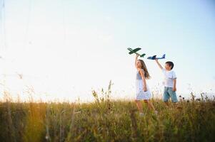 Running boy and girl holding two green and blue airplanes toy in the field during summer sunny day photo