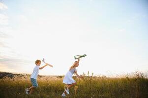 Running boy and girl holding two green and blue airplanes toy in the field during summer sunny day photo