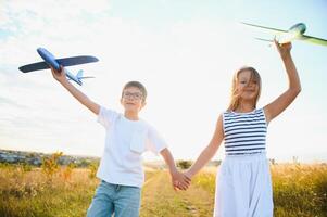 Running boy and girl holding two green and blue airplanes toy in the field during summer sunny day photo